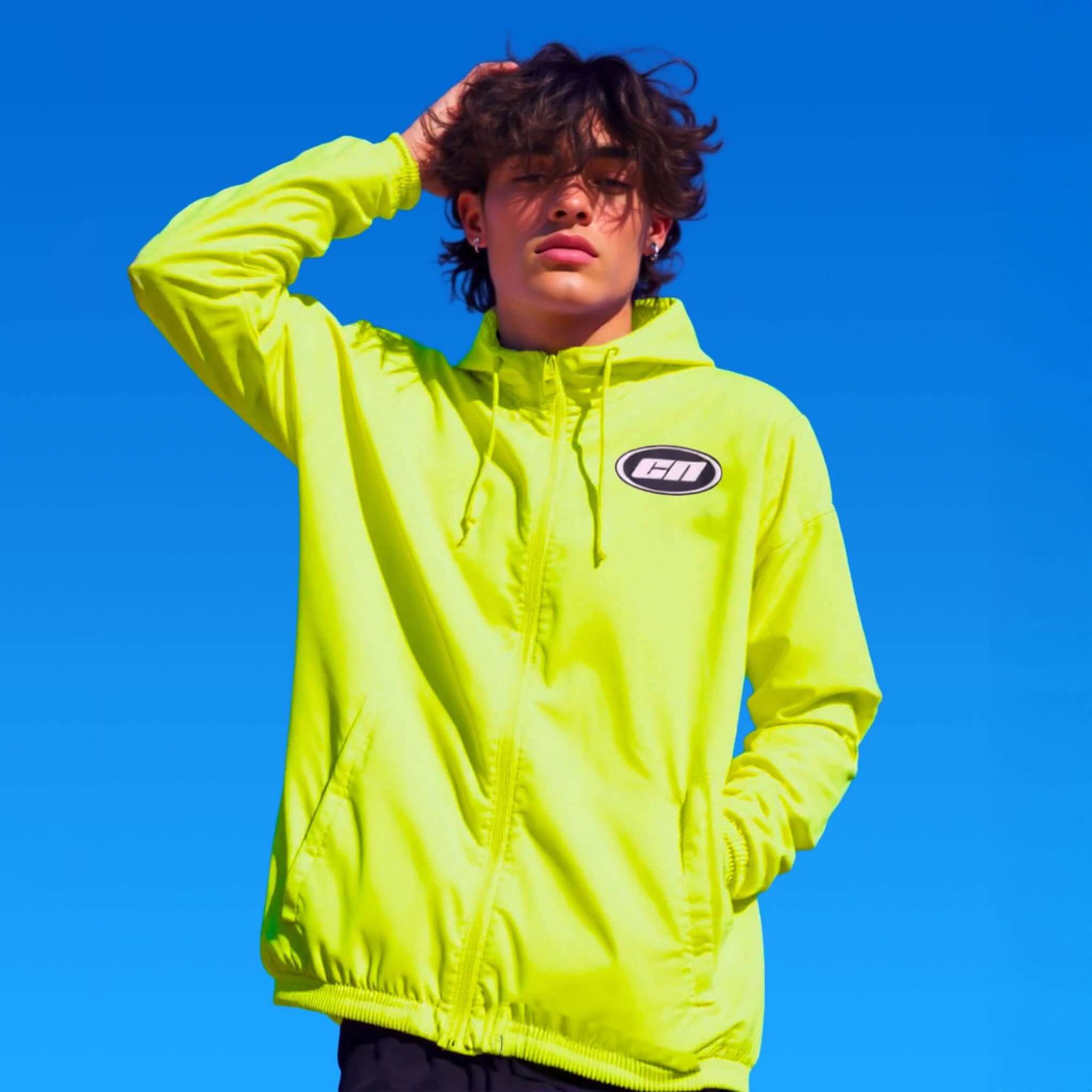 Model wearing a vibrant neon windbreaker against a clear blue sky, showcasing futuristic streetwear style.