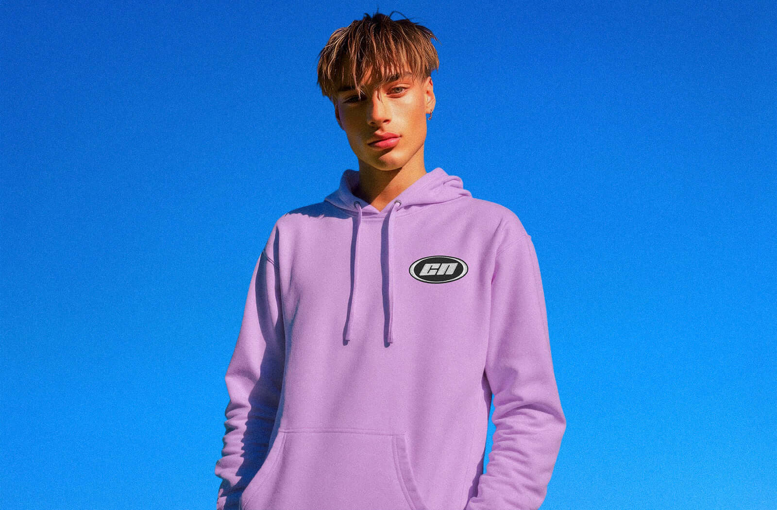 Young man in a lavender hoodie against a blue sky, showcasing casual streetwear style.
