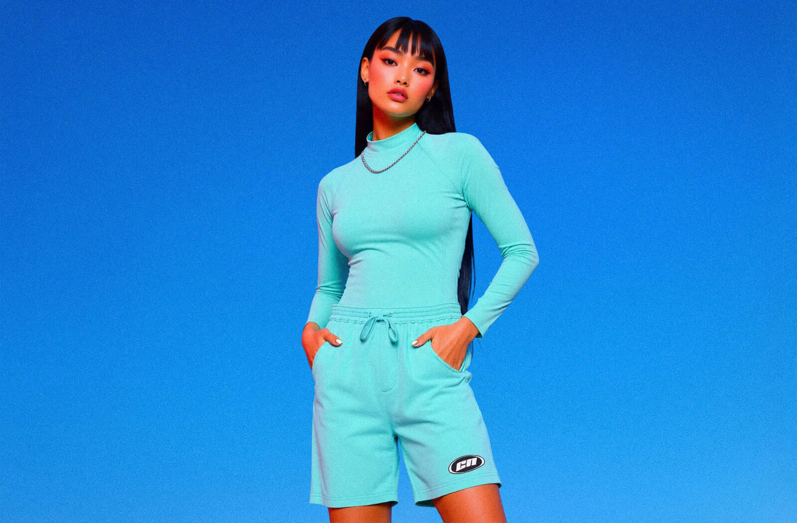 Model showcasing Club Neo aqua blue bottoms in a stylish, structured fit against a vibrant blue background.
