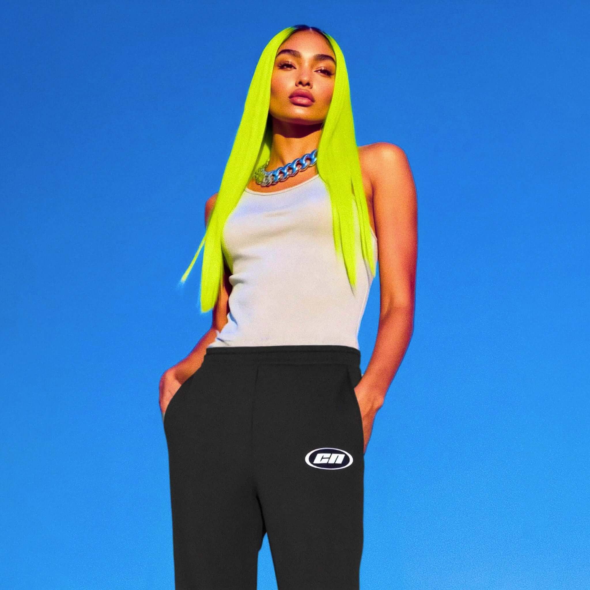 Person with bright green hair wearing a white tank top and black pants with a logo against a blue background