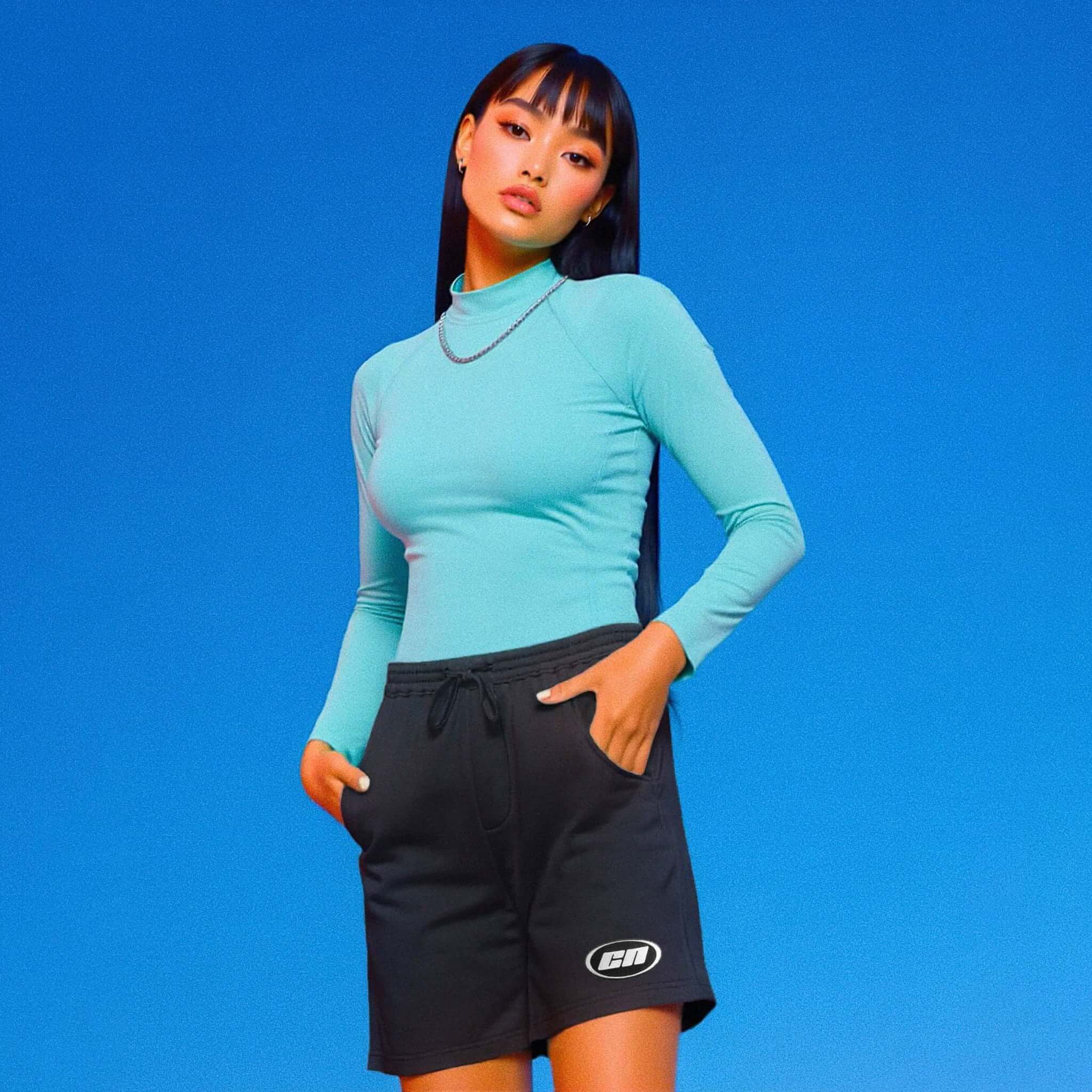 Person wearing a turquoise long-sleeve top and black shorts with a logo on a blue background