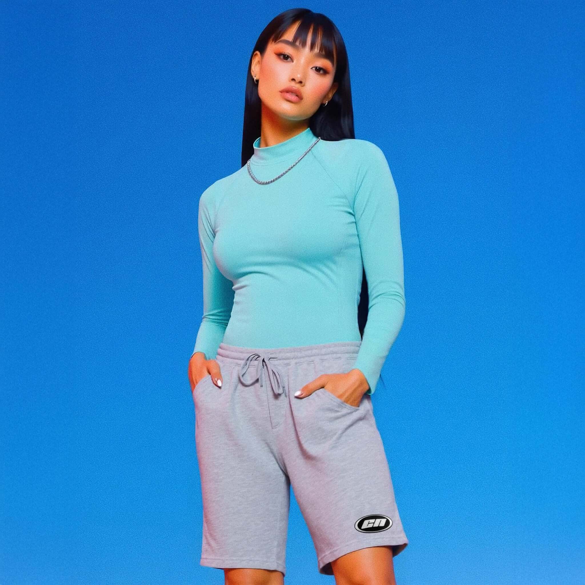 Woman wearing a turquoise long-sleeve top and gray shorts against a blue background