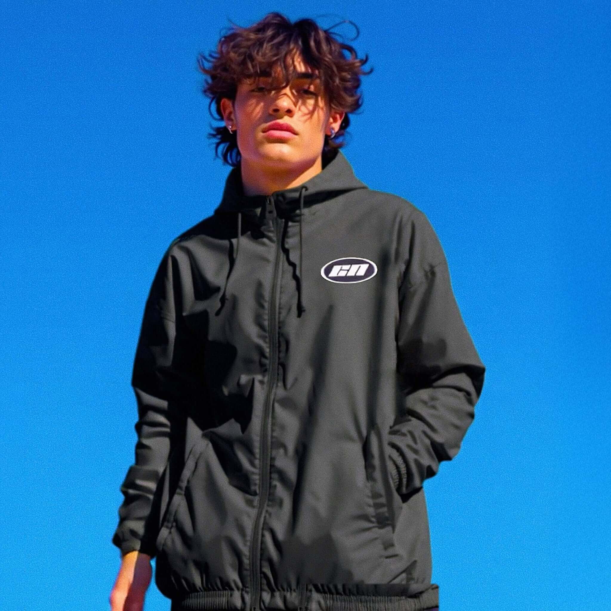 Person wearing a black jacket with a logo against a clear blue sky